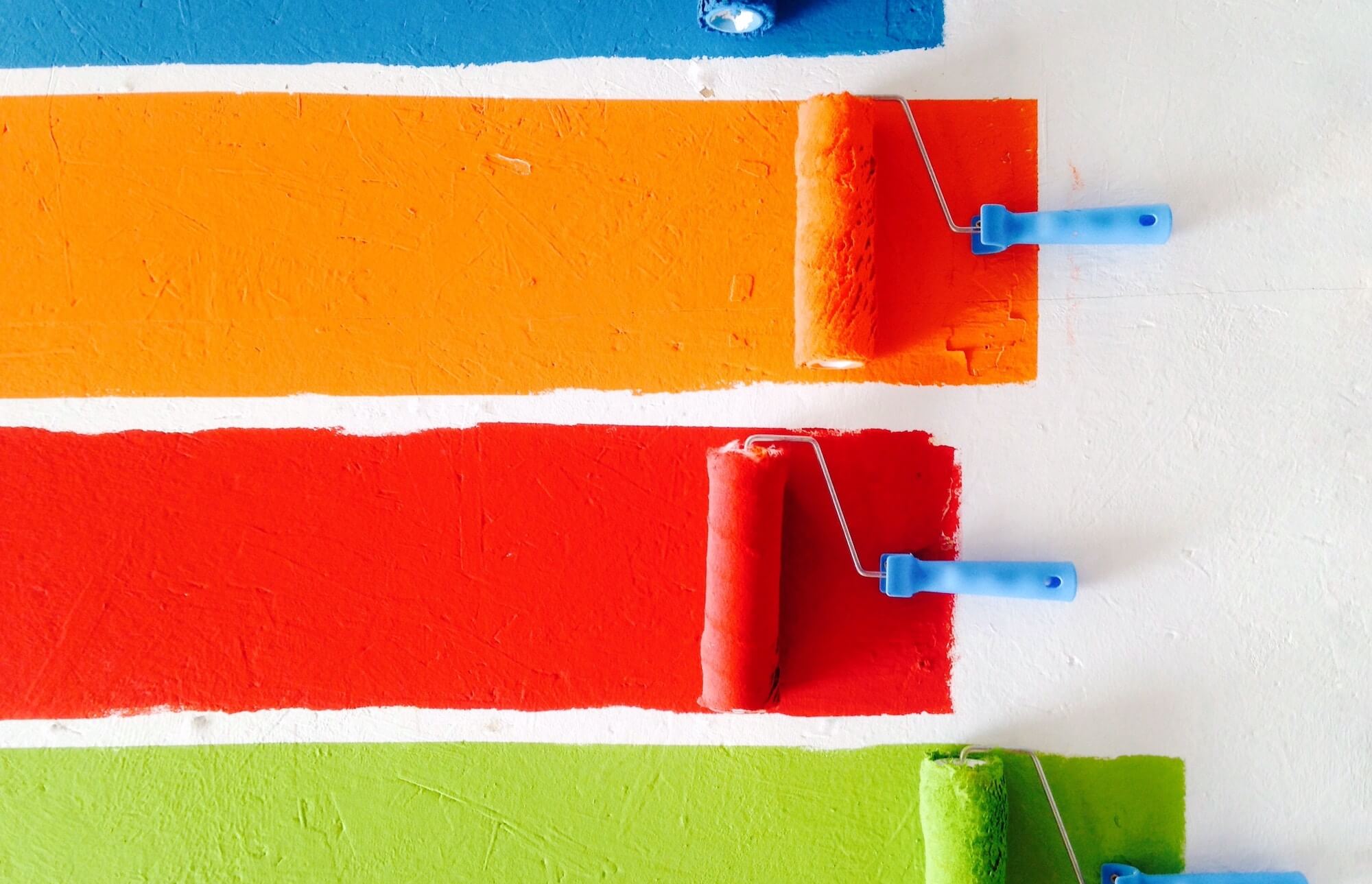 Blue, orange, red and green paint rollers on white